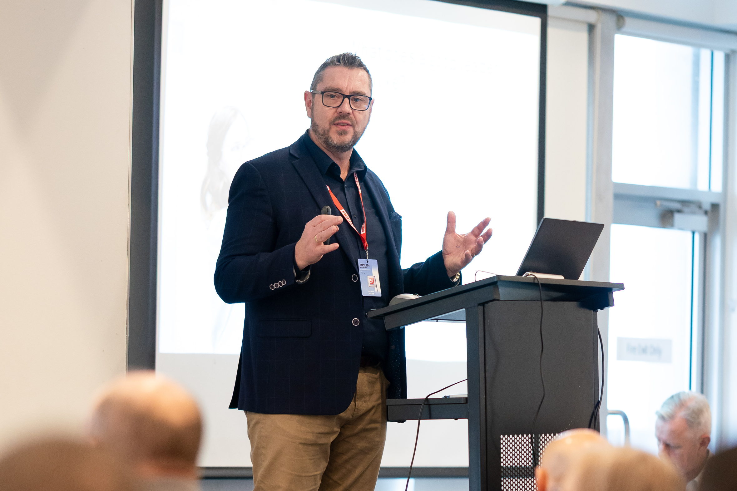 Colin Wilson mid-gesture with both hands raised while delivering an energetic keynote